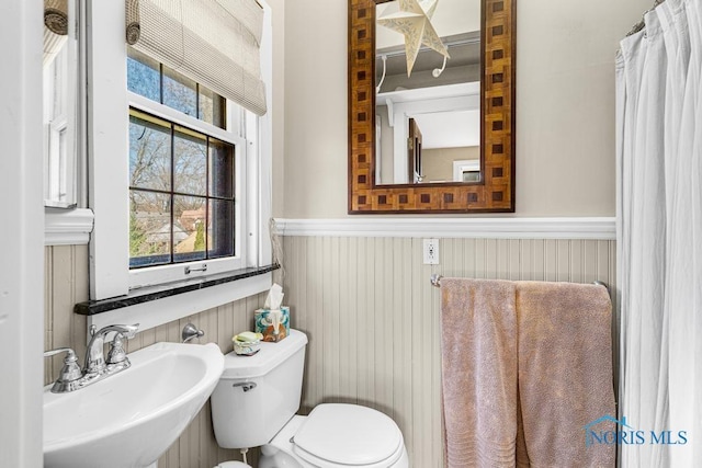 bathroom featuring a wealth of natural light, wainscoting, a sink, and toilet