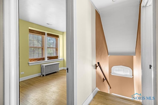 hallway with visible vents, baseboards, an upstairs landing, hardwood / wood-style flooring, and radiator heating unit