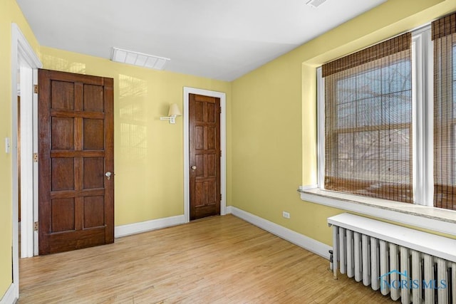 spare room with visible vents, radiator heating unit, wood finished floors, and baseboards