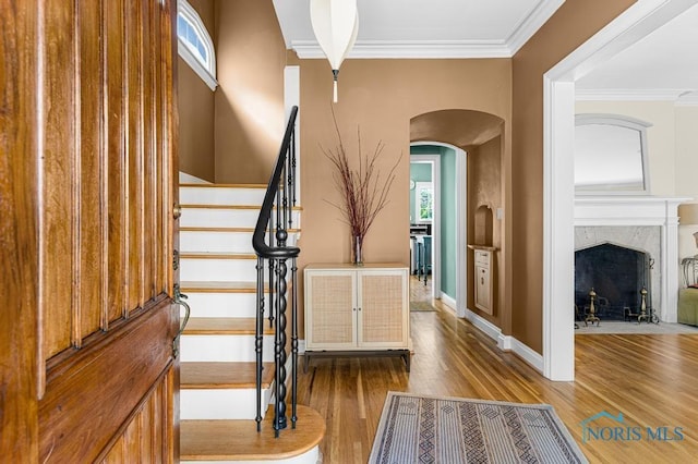 entryway featuring crown molding, a wealth of natural light, arched walkways, stairway, and wood finished floors