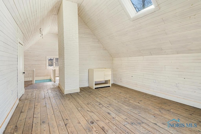 additional living space with vaulted ceiling with skylight, light wood-type flooring, and wood walls