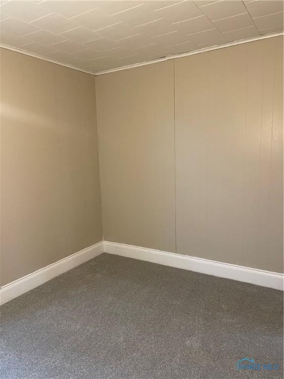 spare room with dark carpet, baseboards, and ornamental molding