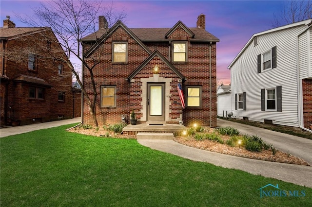 tudor home with roof with shingles, a chimney, a front lawn, and brick siding