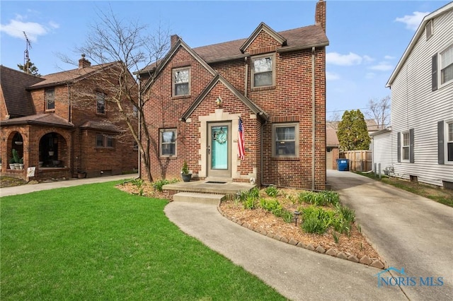 tudor house featuring roof with shingles, a chimney, a front lawn, and brick siding