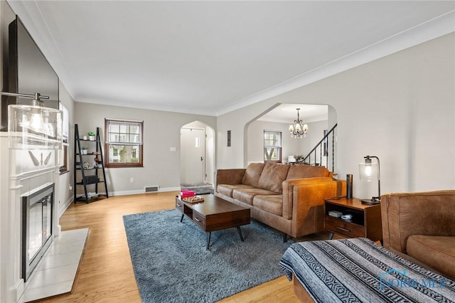 living area featuring visible vents, arched walkways, a notable chandelier, light wood finished floors, and a fireplace with flush hearth