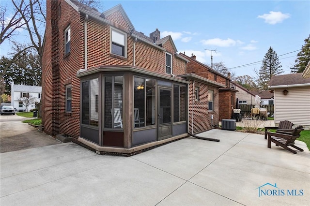back of house with a patio area, brick siding, central air condition unit, and a sunroom