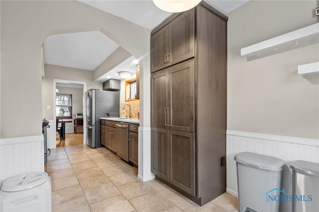 kitchen featuring light tile patterned floors, light countertops, a wainscoted wall, appliances with stainless steel finishes, and a sink