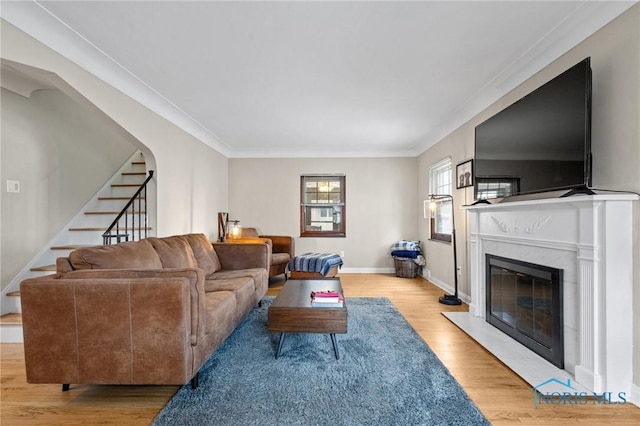 living area featuring baseboards, a fireplace, crown molding, wood finished floors, and stairs