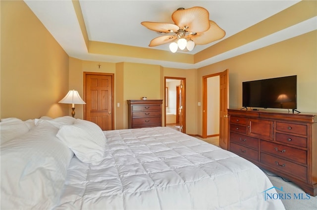 bedroom with ensuite bathroom, baseboards, a raised ceiling, ceiling fan, and light colored carpet