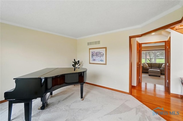 carpeted office with visible vents, baseboards, crown molding, and wood finished floors