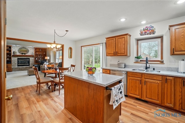 kitchen featuring brown cabinetry, a center island, dishwasher, a sink, and a brick fireplace