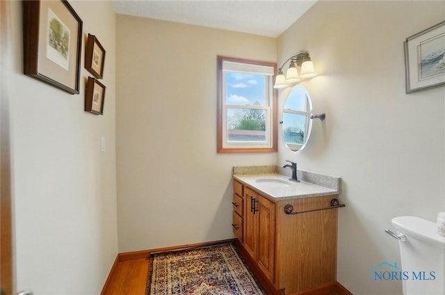 half bathroom featuring toilet, vanity, wood finished floors, and baseboards