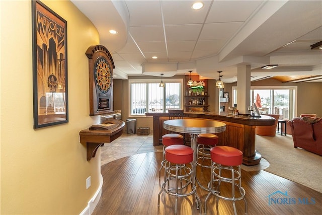 bar with bar area, a healthy amount of sunlight, hanging light fixtures, and wood finished floors