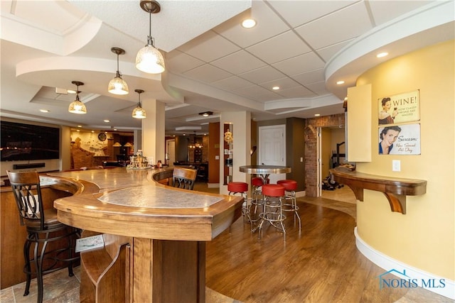 bar featuring wet bar, wood finished floors, a raised ceiling, pendant lighting, and baseboards