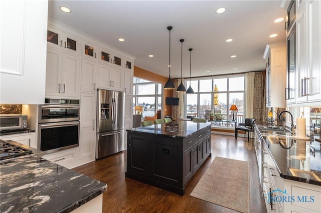 kitchen with a center island, dark stone counters, dark wood finished floors, glass insert cabinets, and appliances with stainless steel finishes