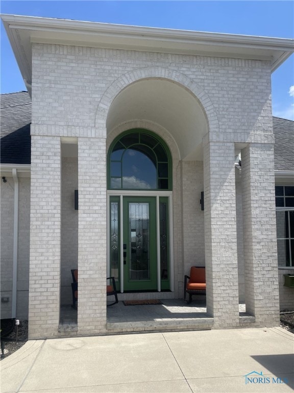 view of exterior entry featuring brick siding and a shingled roof