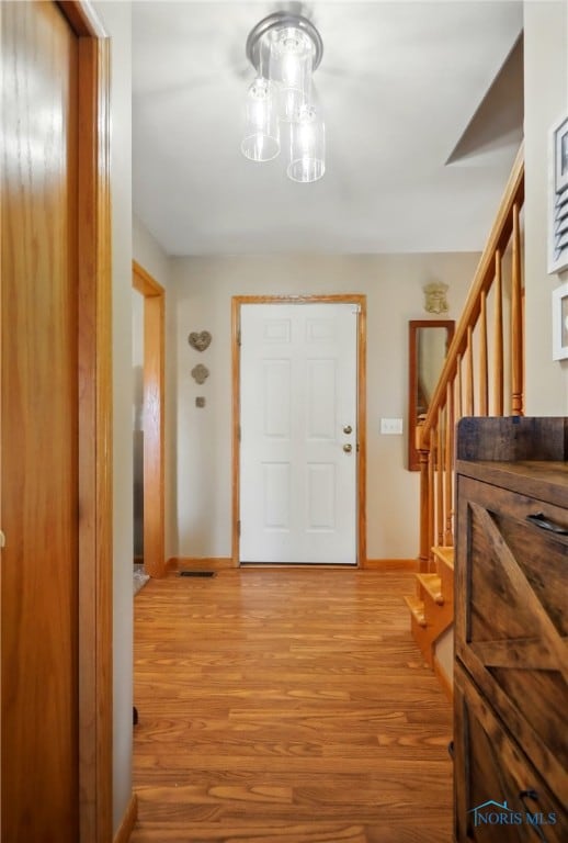 foyer with stairway, baseboards, light wood-type flooring, and an inviting chandelier