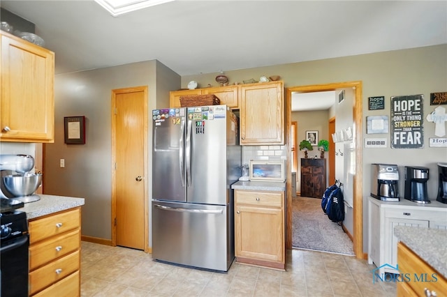 kitchen featuring light brown cabinetry, baseboards, freestanding refrigerator, gas stove, and light countertops