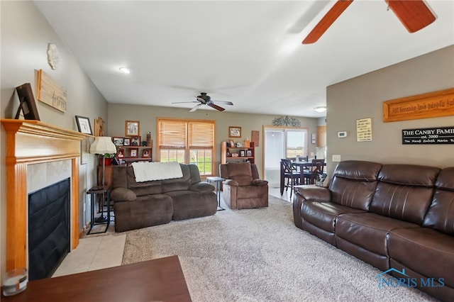 tiled living area with a fireplace with flush hearth, carpet, and a ceiling fan