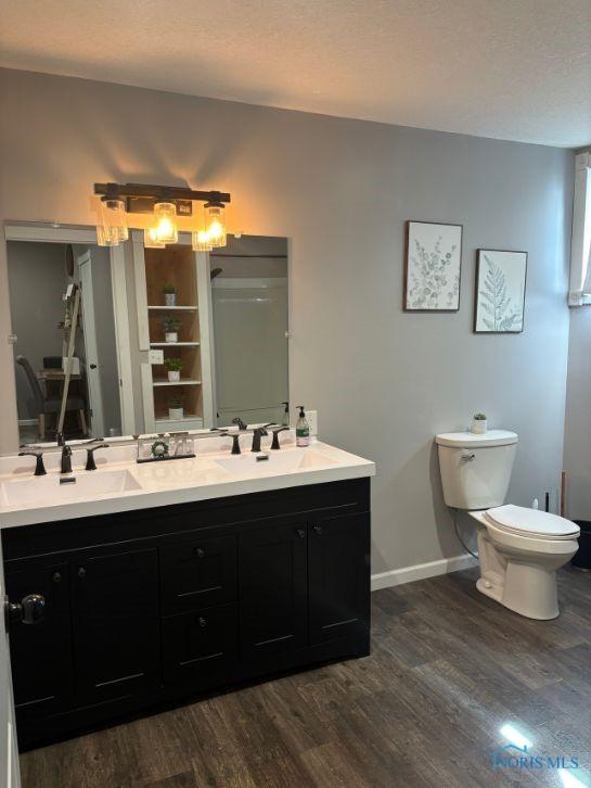 full bathroom featuring toilet, wood finished floors, double vanity, and a sink