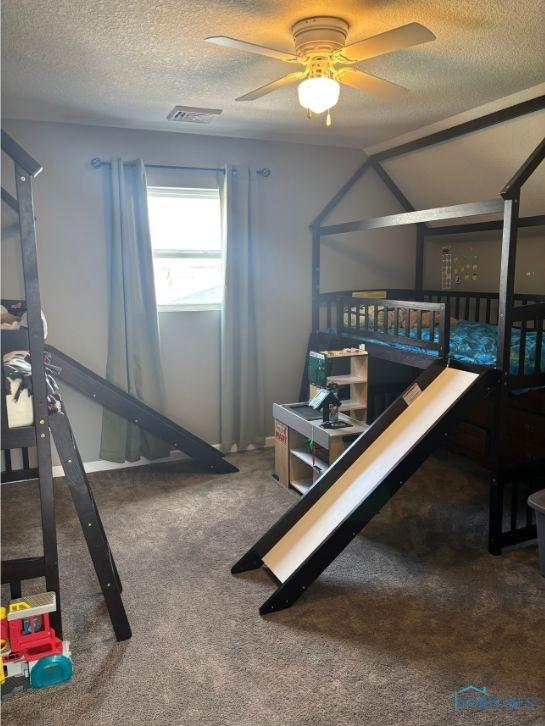 recreation room with a textured ceiling, visible vents, a ceiling fan, and carpet