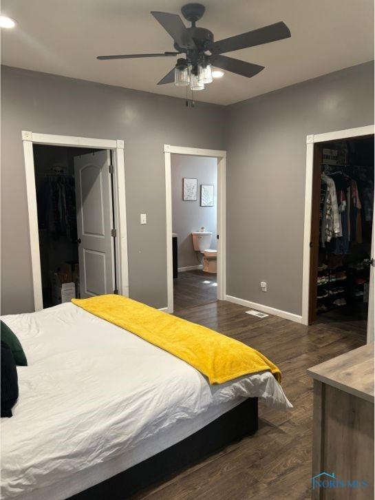bedroom featuring a closet, baseboards, ensuite bathroom, a walk in closet, and dark wood-type flooring