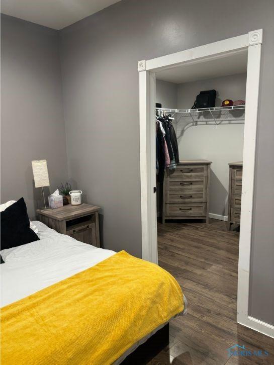 bedroom with a spacious closet, a closet, baseboards, and wood finished floors