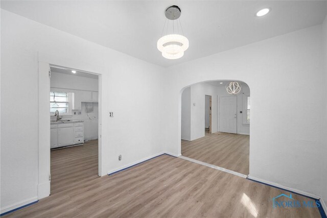 3251 Cottage Ave, Toledo, OH 43608 - unfurnished dining area featuring arched walkways, a chandelier, light wood finished floors, and baseboards