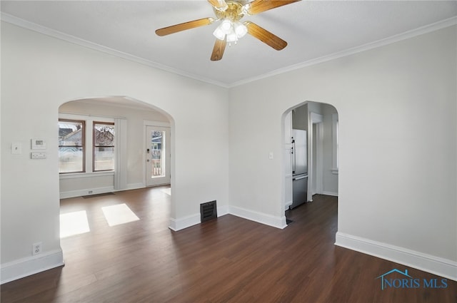 spare room featuring wood finished floors, visible vents, a ceiling fan, ornamental molding, and arched walkways