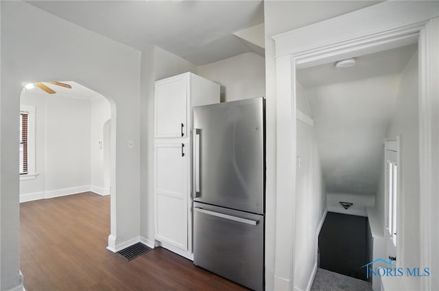 kitchen featuring arched walkways, dark wood finished floors, baseboards, white cabinetry, and freestanding refrigerator