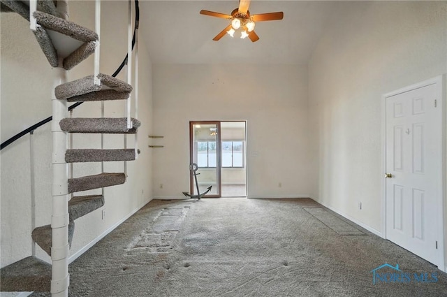 unfurnished living room featuring a towering ceiling, ceiling fan, baseboards, and carpet floors
