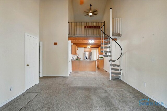 unfurnished living room featuring light carpet, stairs, a high ceiling, and ceiling fan