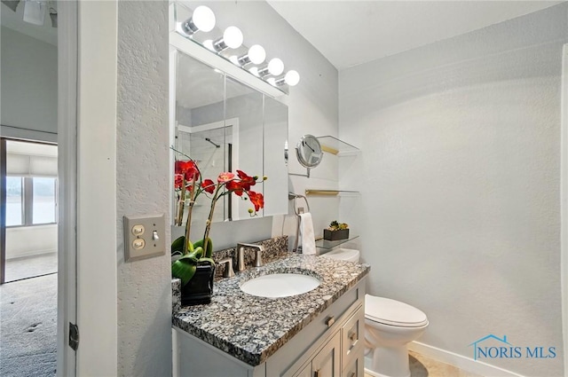 bathroom featuring a textured wall, vanity, baseboards, and toilet