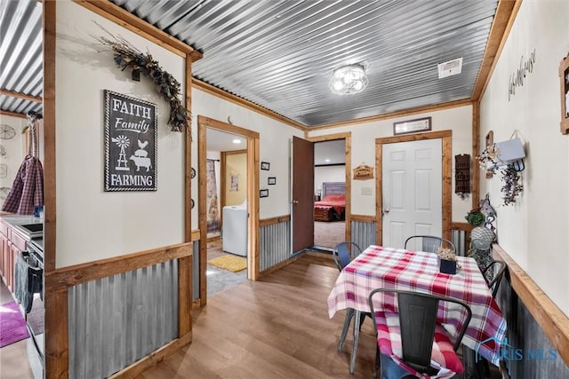 dining space with a wainscoted wall, wood finished floors, and ornamental molding