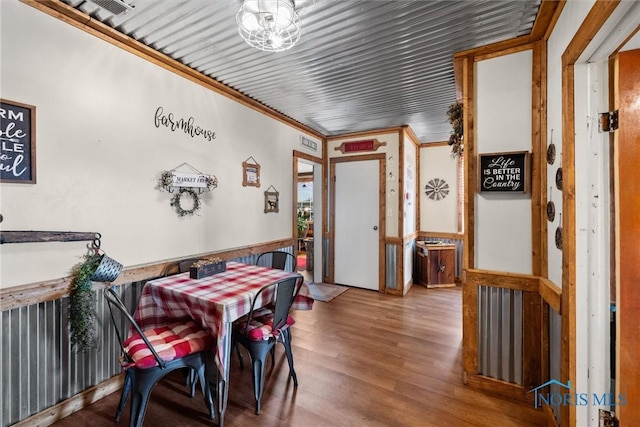 dining room featuring wood finished floors, crown molding, and a wainscoted wall