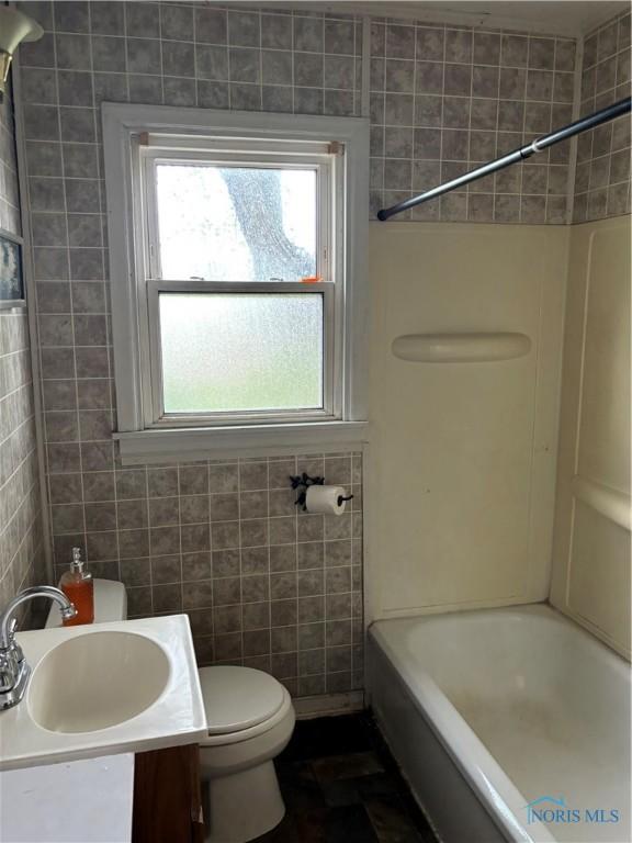 full bath with vanity,  shower combination, toilet, and tile walls