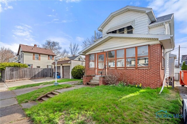 view of front of property with a detached garage, a front yard, brick siding, an outbuilding, and fence