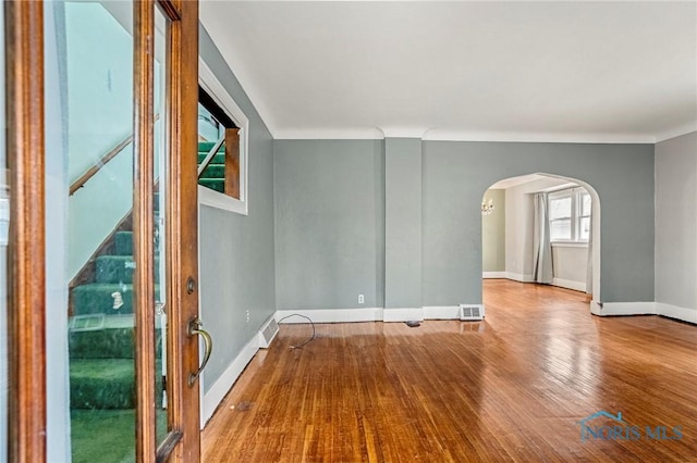 spare room featuring arched walkways, visible vents, baseboards, and wood finished floors