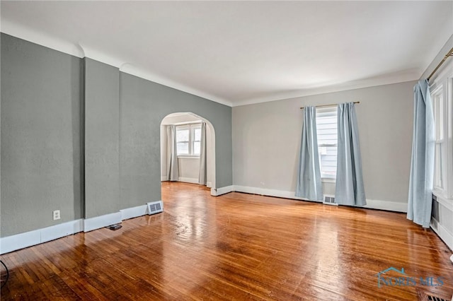 empty room with visible vents, baseboards, arched walkways, and wood finished floors