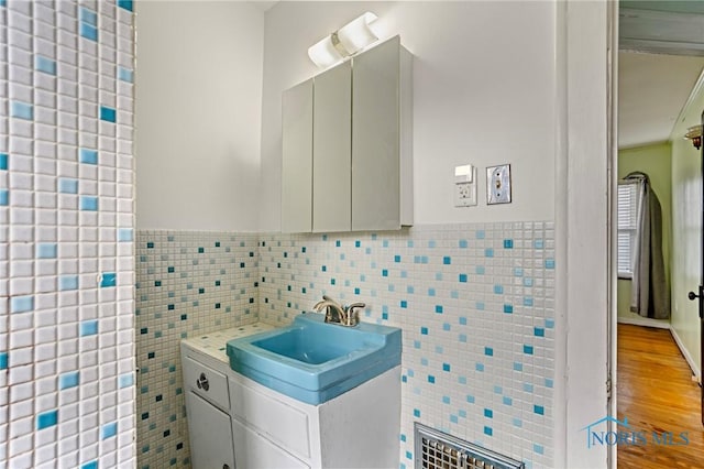 bathroom with wood finished floors, vanity, wainscoting, and tile walls