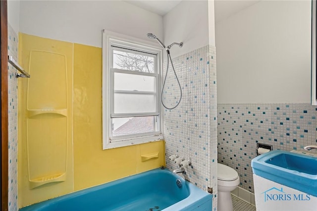 bathroom featuring a sink, tile walls, toilet, bathtub / shower combination, and wainscoting