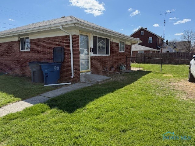 back of property featuring brick siding, a yard, and fence