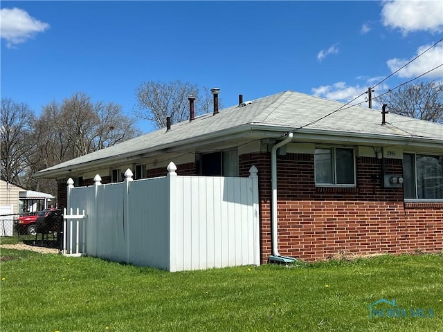view of side of home featuring fence, brick siding, and a yard