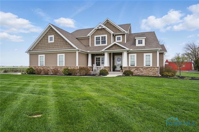 craftsman house featuring a porch, stone siding, a shingled roof, and a front yard