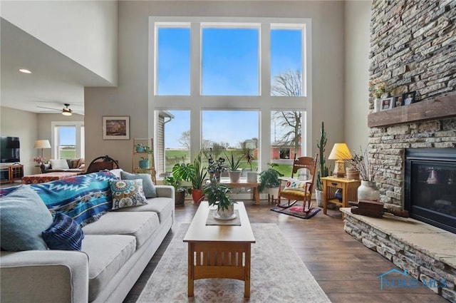 living room featuring a ceiling fan, wood finished floors, a fireplace, a high ceiling, and recessed lighting