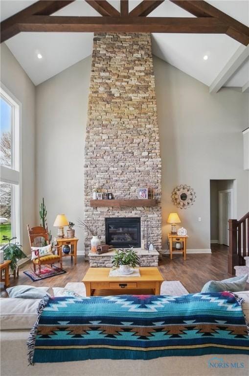 living area with beam ceiling, baseboards, wood finished floors, a stone fireplace, and high vaulted ceiling