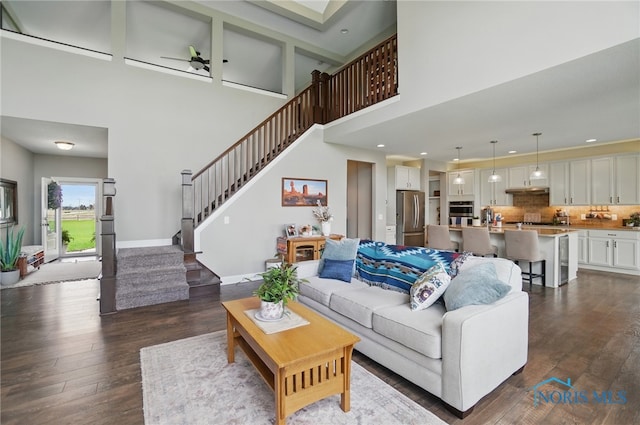 living area with baseboards, a towering ceiling, recessed lighting, stairs, and dark wood-type flooring
