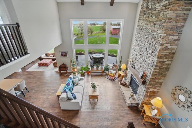 living area featuring wood finished floors, a towering ceiling, beamed ceiling, and a fireplace