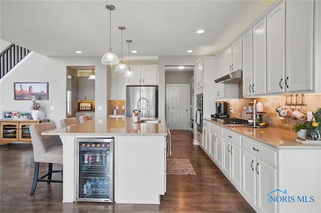 kitchen featuring wine cooler, a kitchen breakfast bar, recessed lighting, white cabinetry, and under cabinet range hood