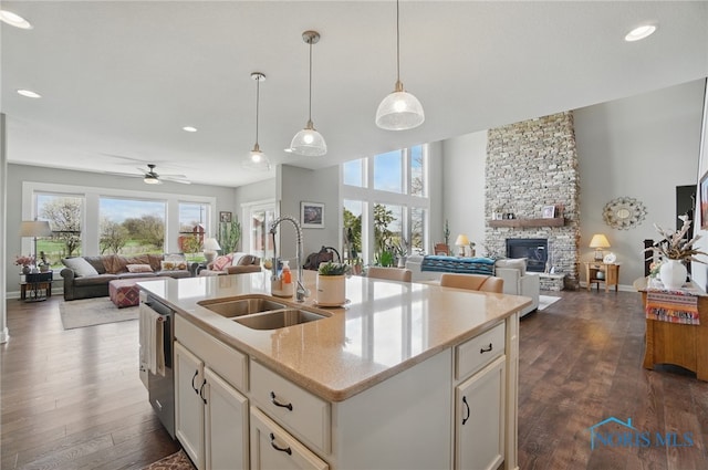 kitchen with stainless steel dishwasher, a sink, open floor plan, a fireplace, and dark wood finished floors